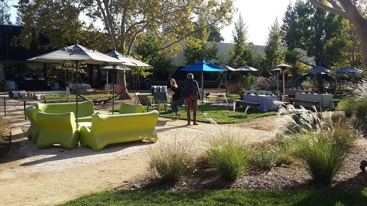 Googleplex kampüsünde yeşil koltuklar, masalar ve şemsiyeler