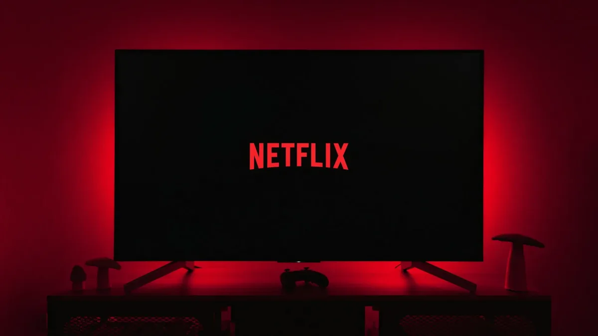 Kırmızı ışıklı odada Netflix logosunu gösteren televizyon ve önündeki oyun kumandası